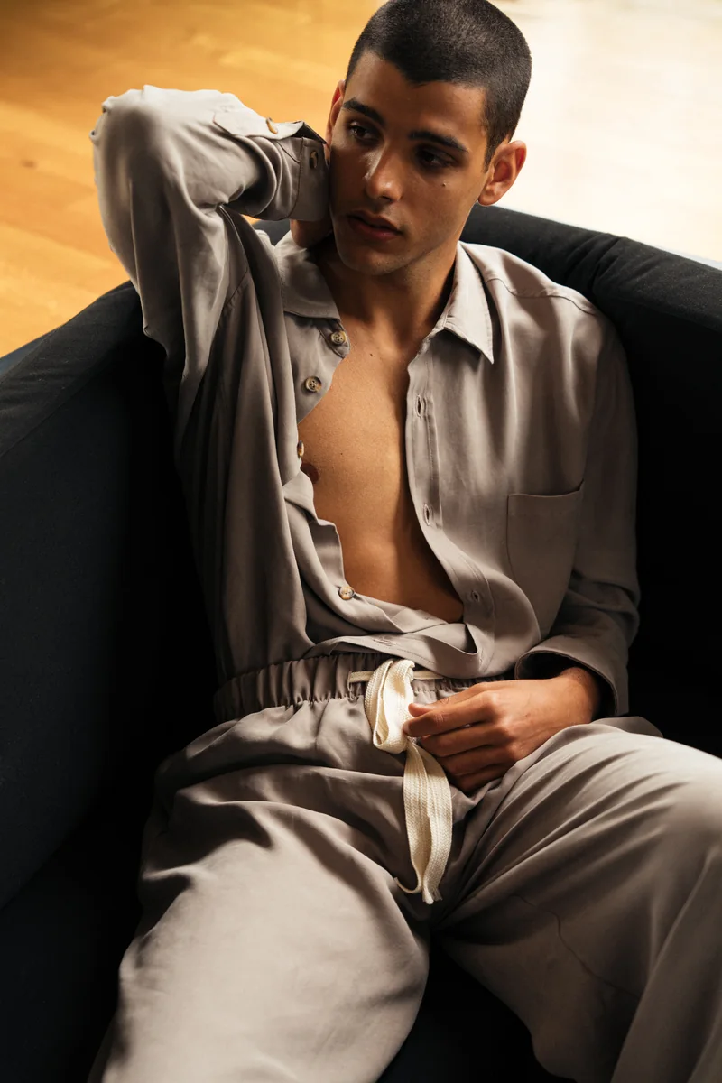 Close portrait of a model in a taupe relaxed shirt and drawstring trousers seated on a black sofa