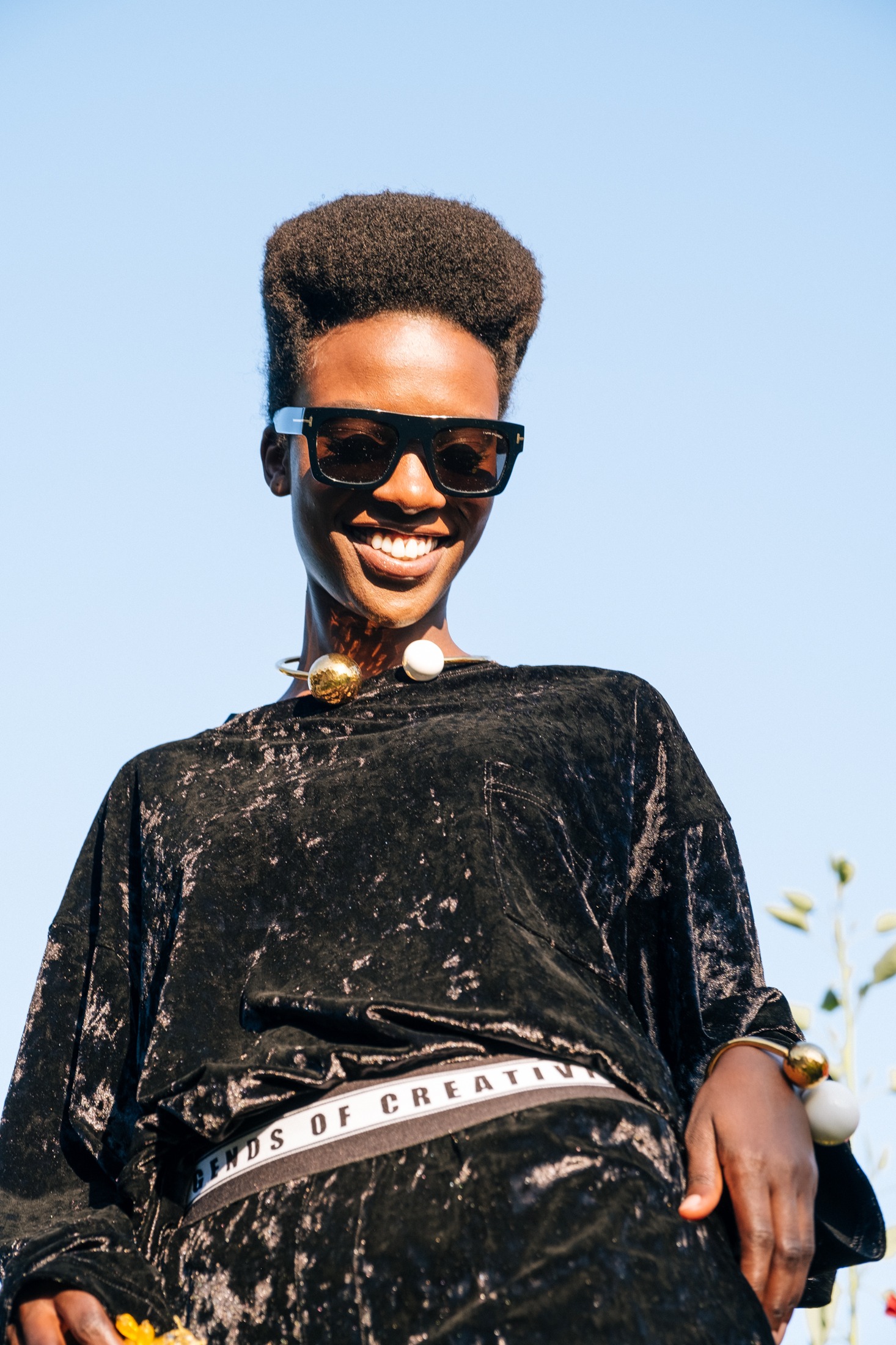 Portrait of a model in a black crushed-velvet set with the Legends of Creativity waistband, photographed against clear sky
