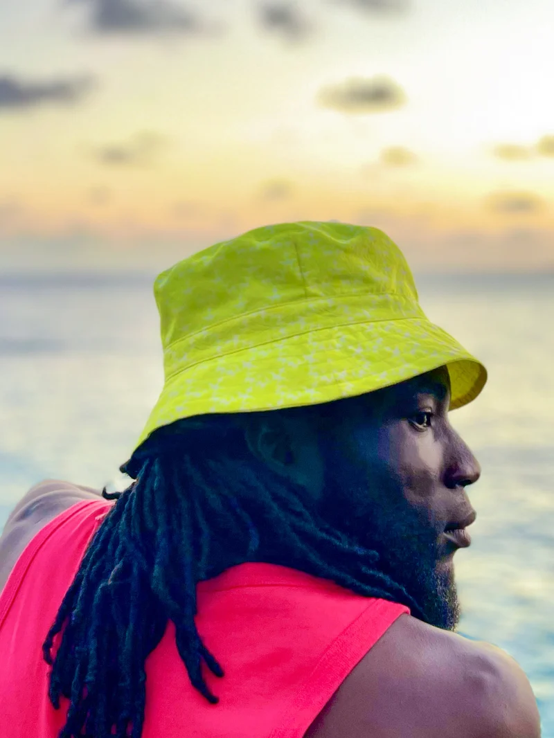 Side portrait of a model in a yellow bucket hat with the ocean behind