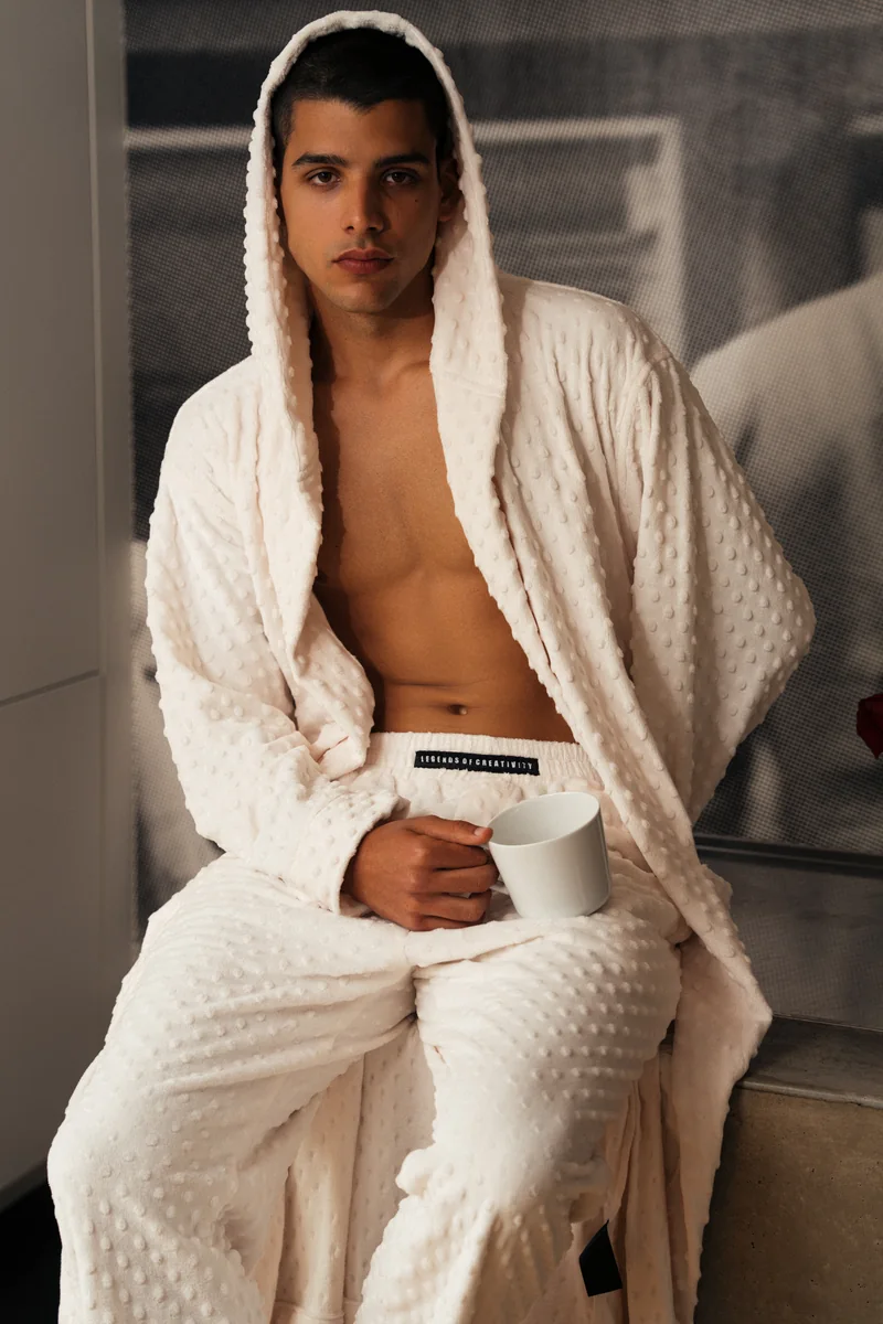 Close portrait of a model in a white textured hooded robe and matching trousers, holding a white mug