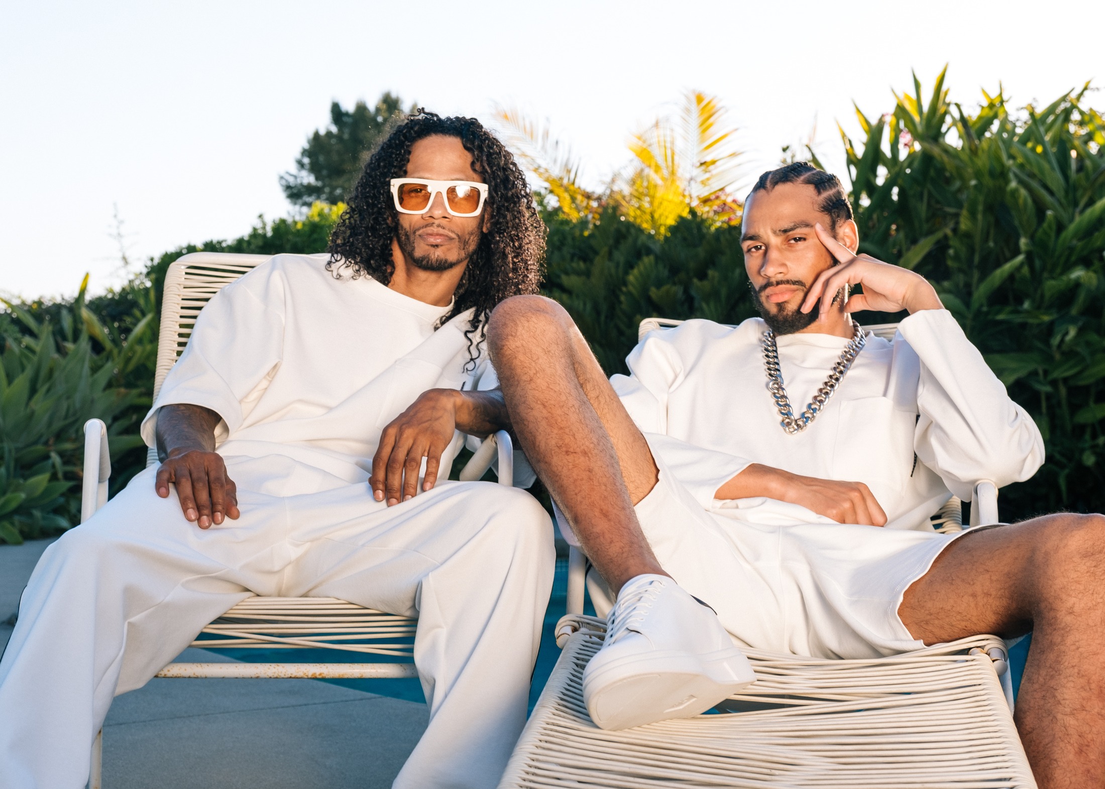 Two models in all-white LOC sets reclining on poolside loungers at golden hour