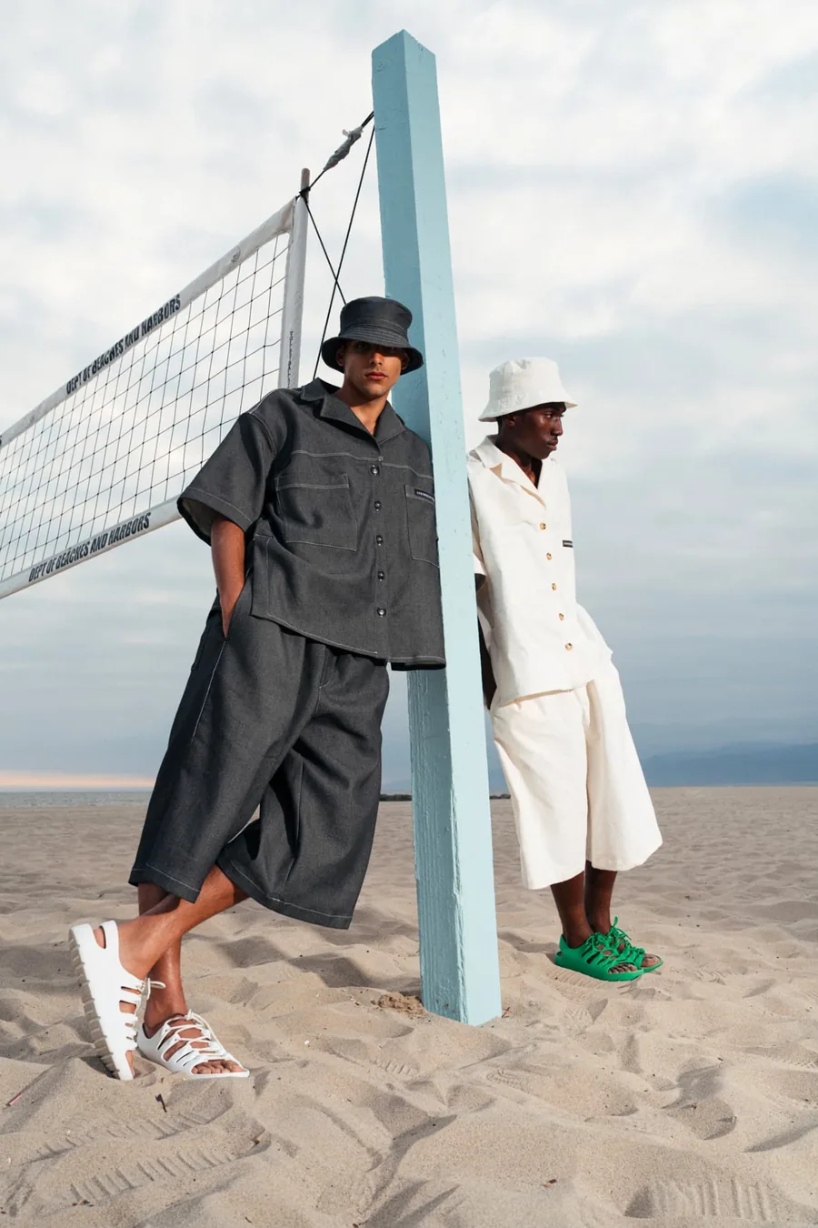 Two models in Luxe Sojourn looks beside a beach volleyball net