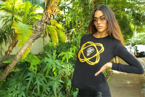 Miami campaign model in a black sweatshirt with a gold graphic, photographed among greenery