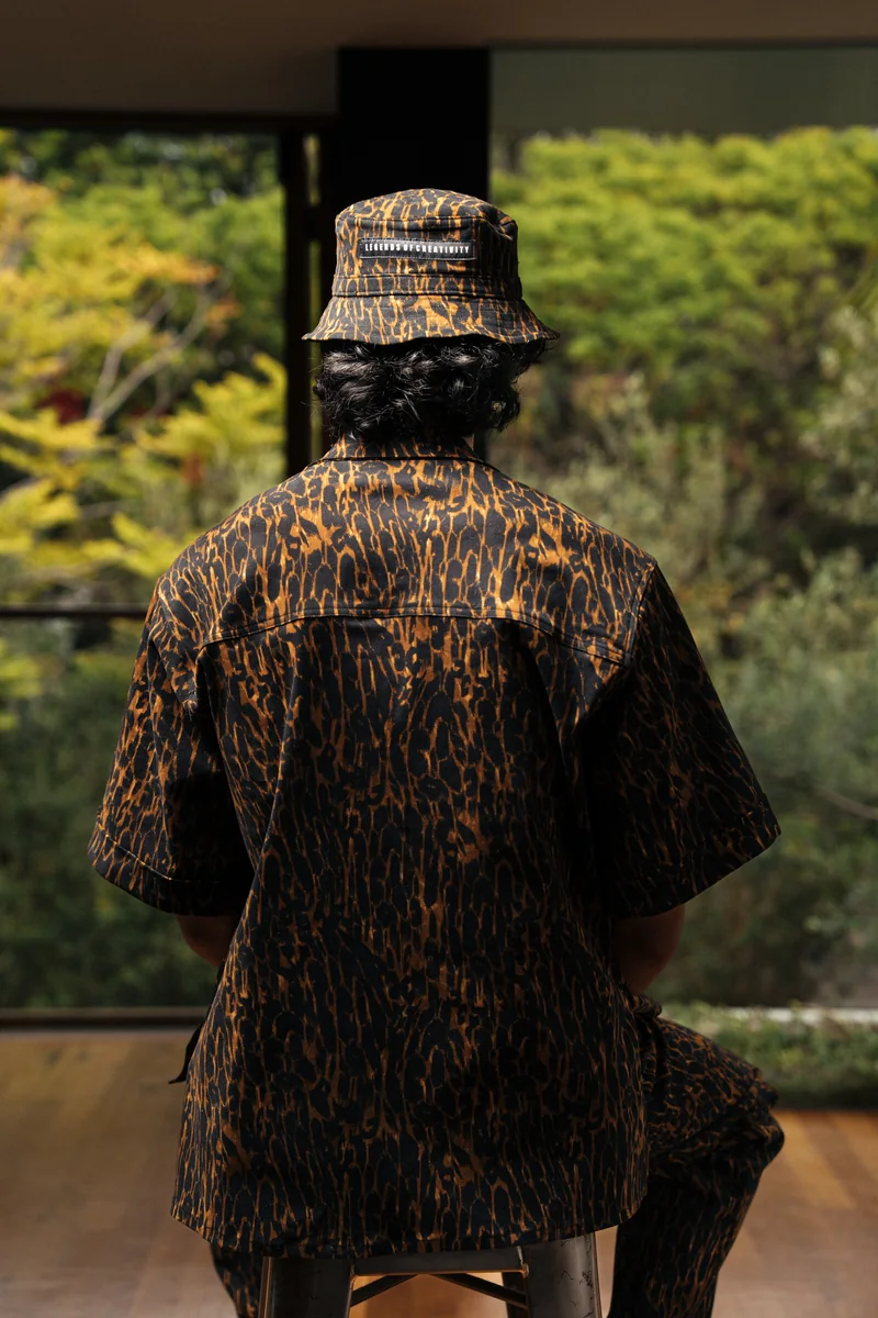 Back view of a model in a leopard-print short-sleeve shirt and matching bucket hat, garden beyond the window