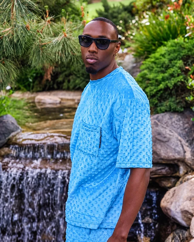 Model in a blue textured outfit standing beside a waterfall