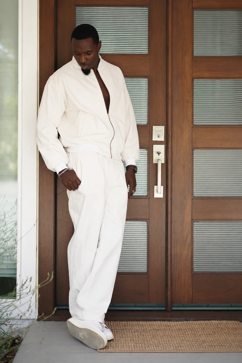Model wearing a chalk corduroy jacket and pants with white shoes in front of wooden double doors