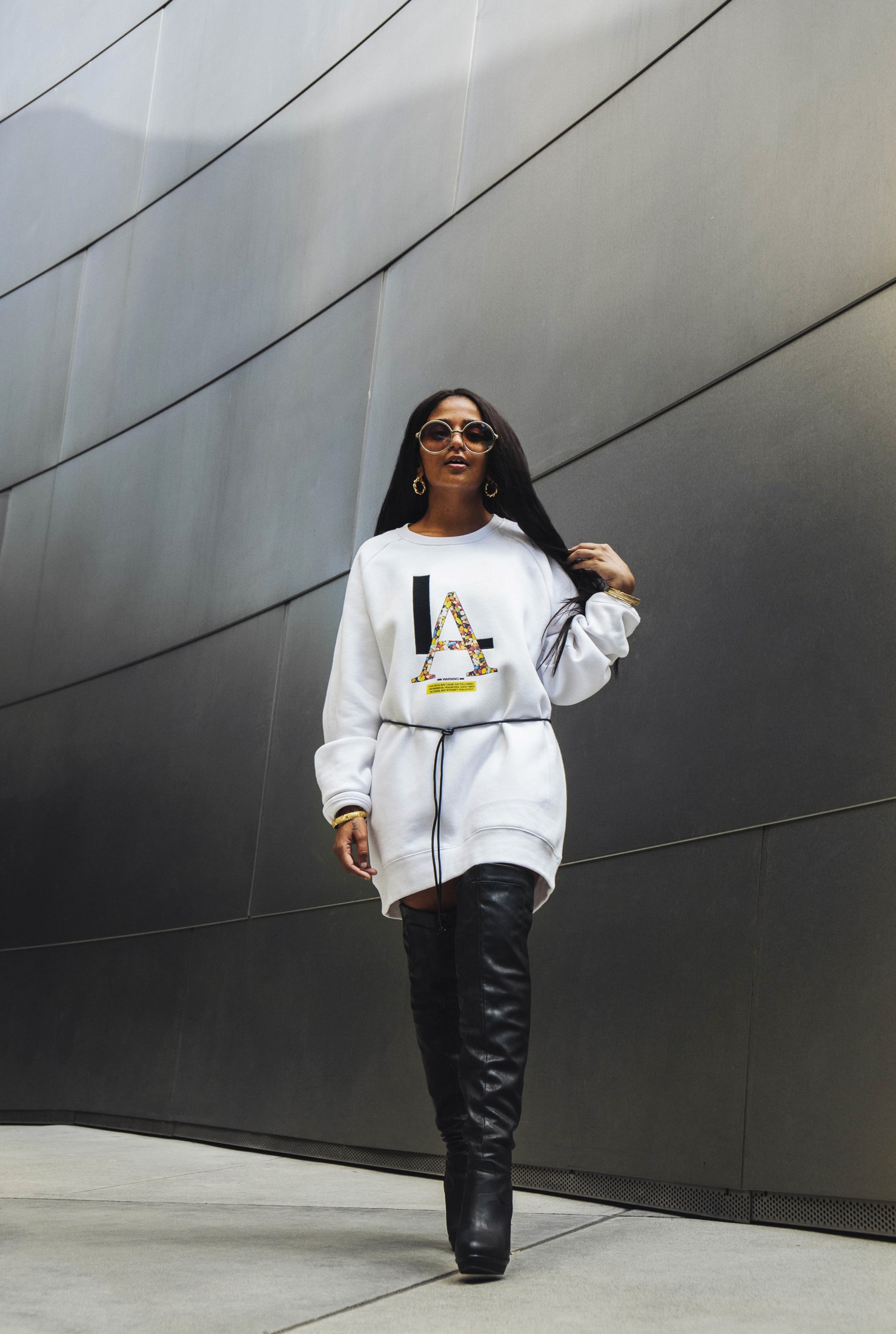 Model in a white graphic top and black boots against an angular metal wall