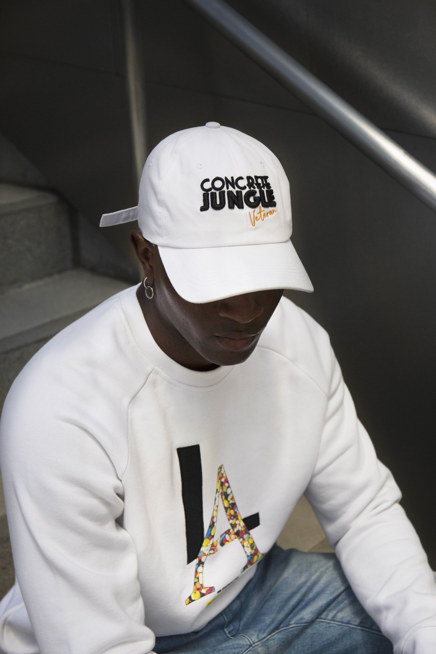 Seated model wearing a white graphic top and white cap