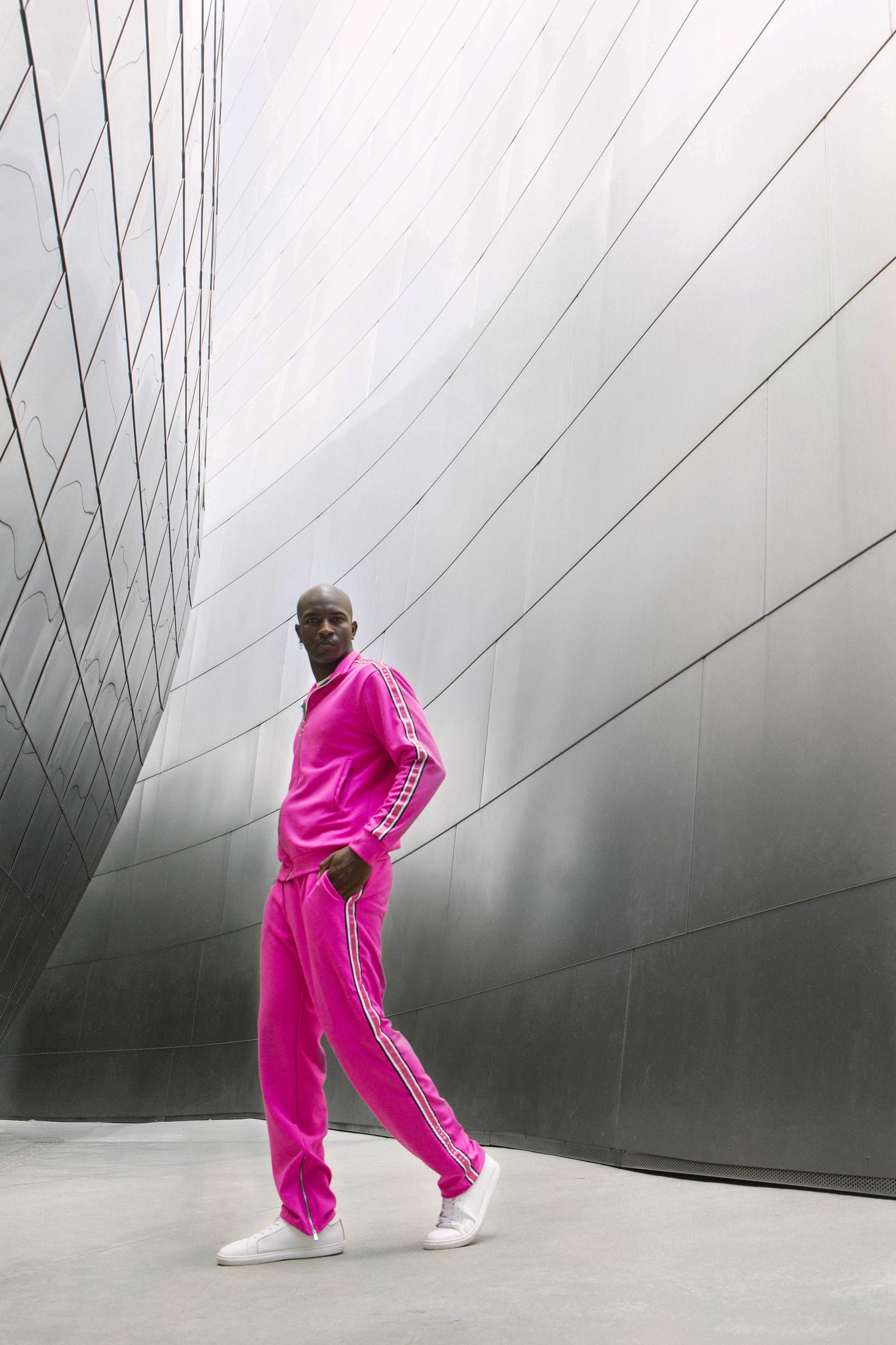 Model in a bright pink LOC tracksuit walking beside a curved metal wall