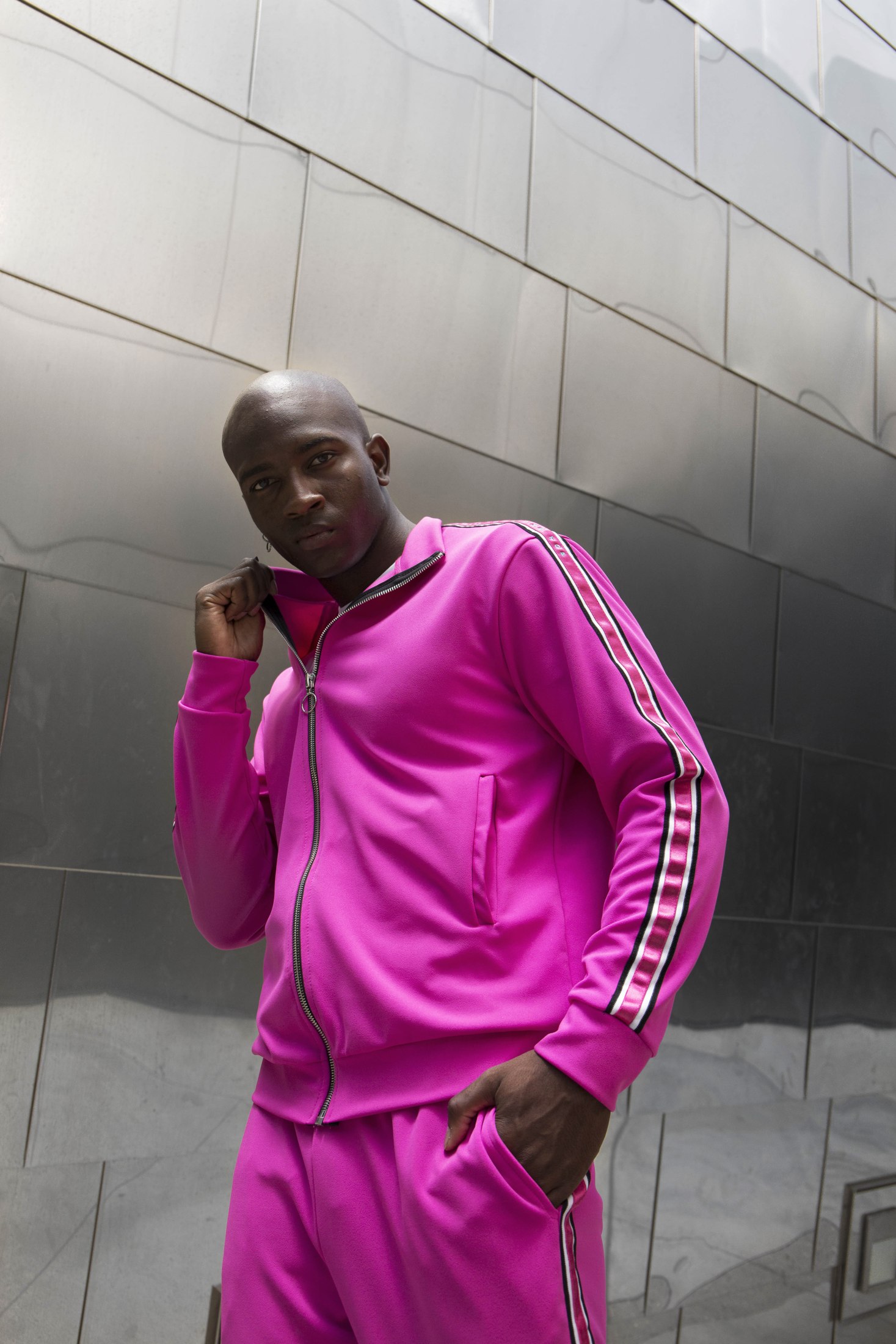 Model in a bright pink LOC tracksuit leaning against a metal wall