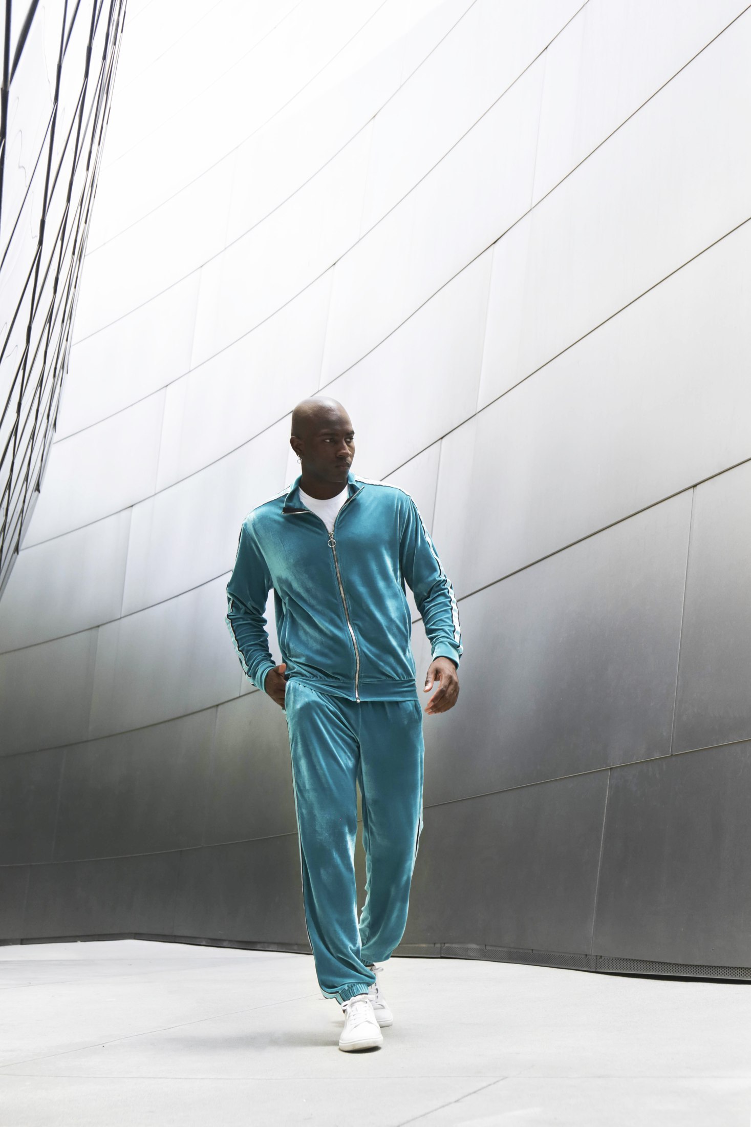 Model in a turquoise LOC tracksuit walking along a curved metal wall