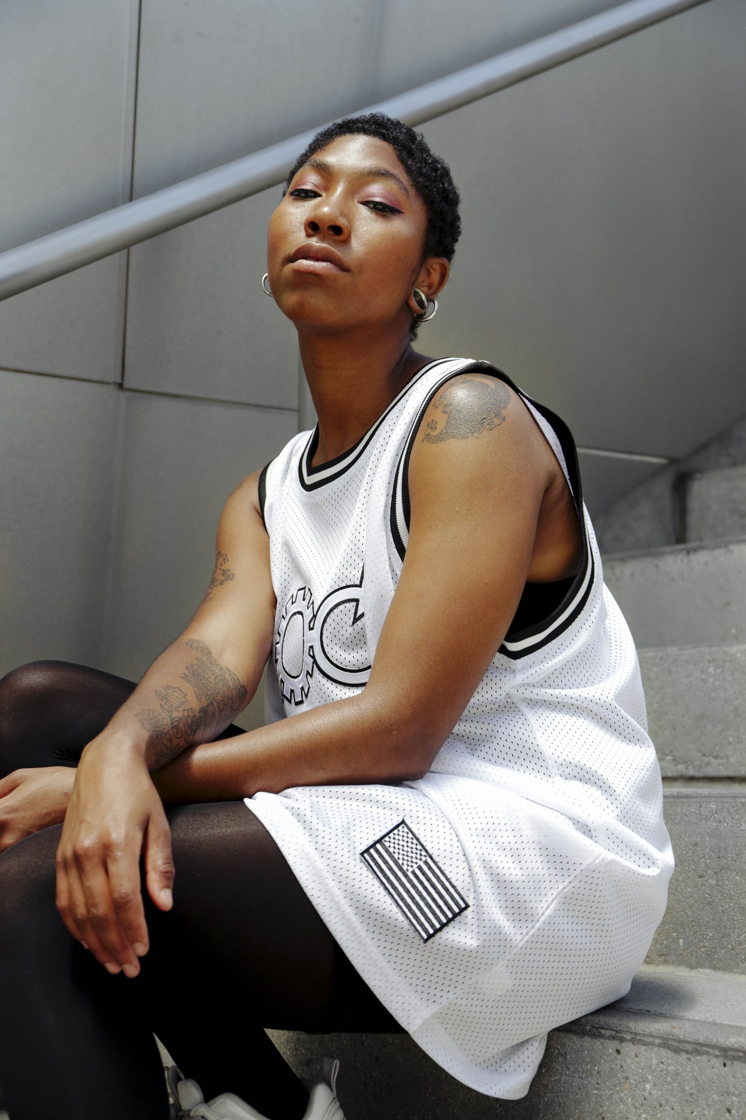 Seated model wearing a white LOC basketball jersey and dark trousers